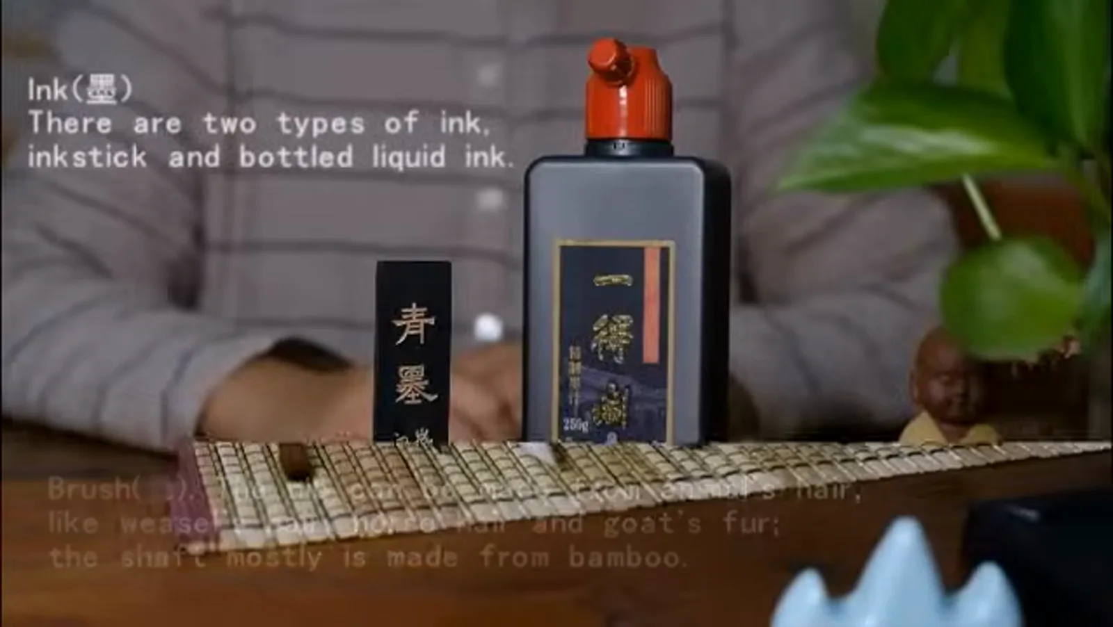 a solid inkstick in its box beside a bottle of liquid ink and a bamboo-shaft brush showing the four treasures of the study for writing a Chinese name