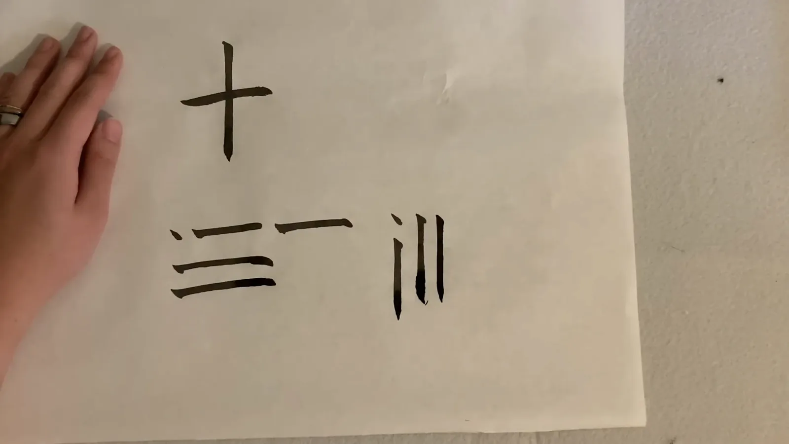 A beginner calligraphy practice sheet showing the characters shi ten, san three and chuan river written with fine-tipped brush strokes A beginner calligraphy practice sheet showing the characters shi ten, san three and chuan river written with fine-tipped brush strokes