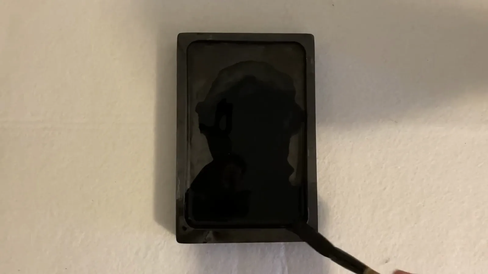 A calligraphy brush being flipped and soaked in freshly ground ink inside a stone inkstone so the bristles take up ink down to the center A calligraphy brush being flipped and soaked in freshly ground ink inside a stone inkstone so the bristles take up ink down to the center